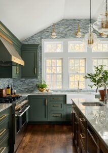 Kitchen with large windows; green cabinetry; green blue variegated tile mosaic backsplash up to vaulted ceiling