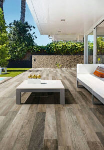 Outdoor patio with woodlook tile, white coffee table, white sofa, and part of a yard visible