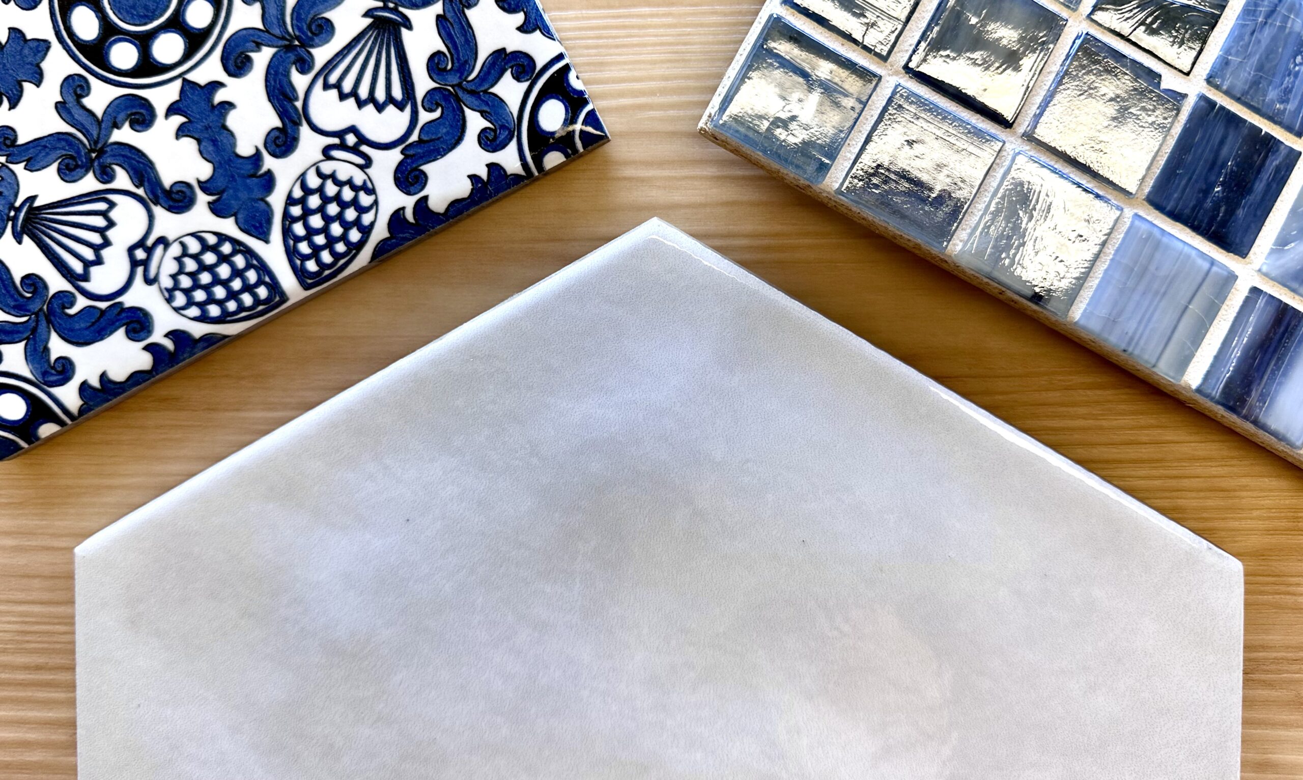 Three tiles, one blue and white patterned, one white hexagon, and one various blue glass squares