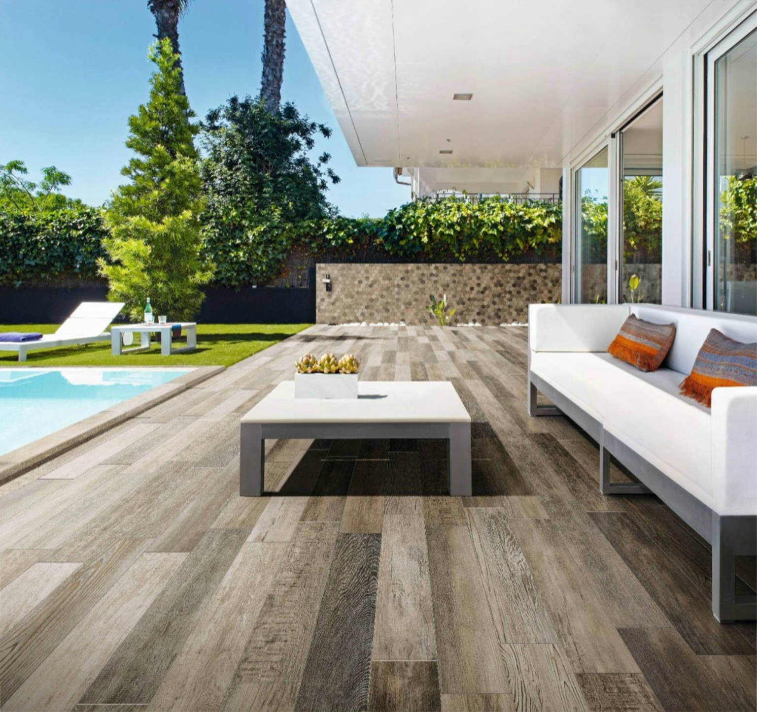 Outdoor patio with woodlook tile, white coffee table, white sofa, and part of a yard visible